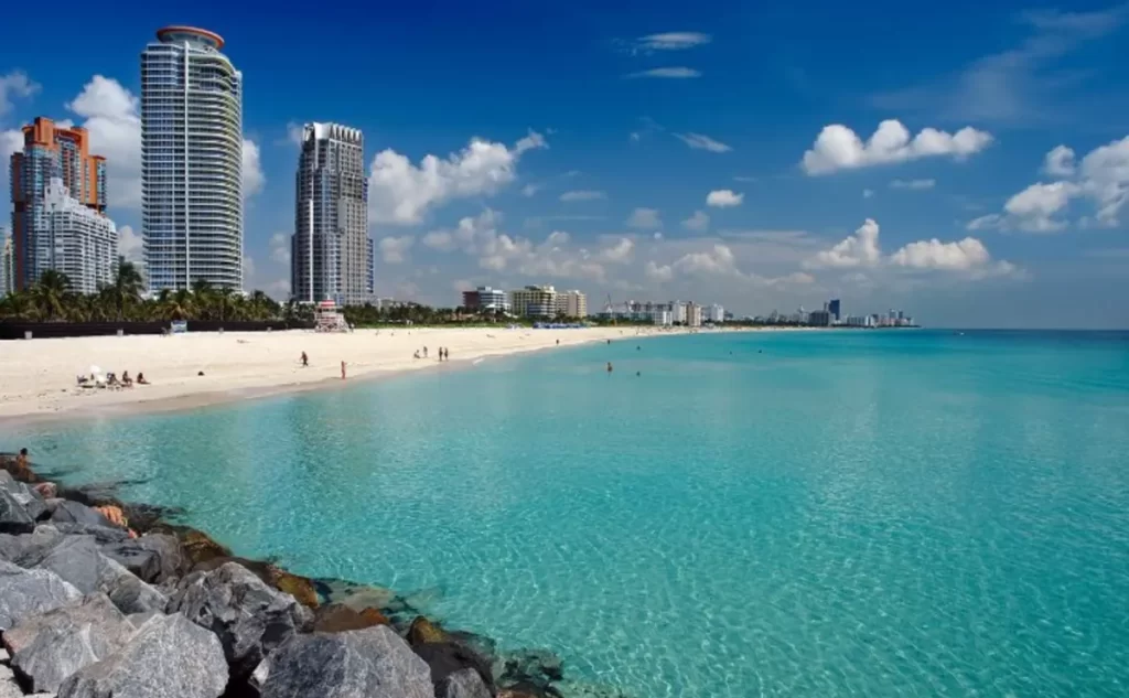 Praia de Miami Beach com mar azul-turquesa, areia branca e prédios à beira-mar na Flórida
